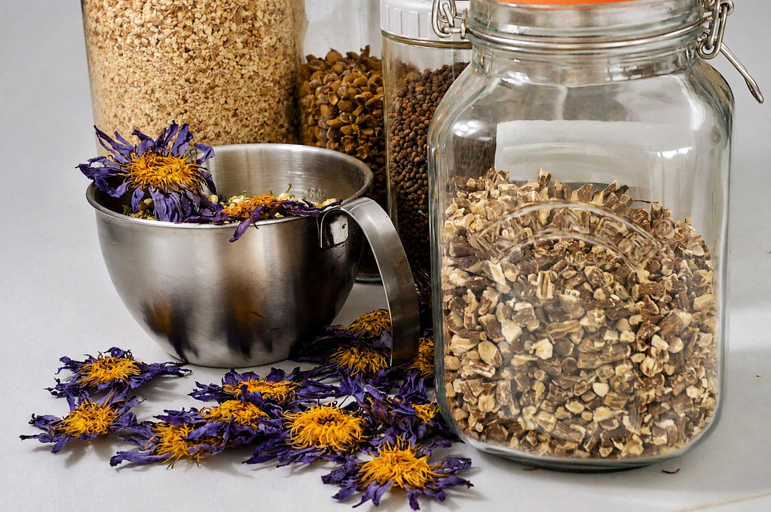 Dried blue lotus flowers in a steel measuring cup beside glass jars of oats, seeds and chopped roots at Herbal Monkey, the UK's independent herbal apothecary